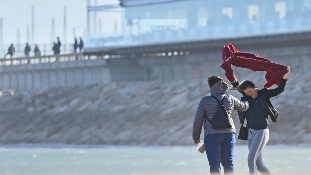 Dos personas se protegen de las fuertes rachas de viento en la playa de Las Arenas de Valencia